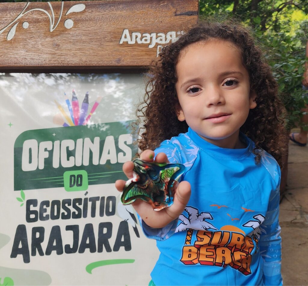 Criança em frente à placa do Geossítio Arajara segurando uma pequena escultura de gesso.